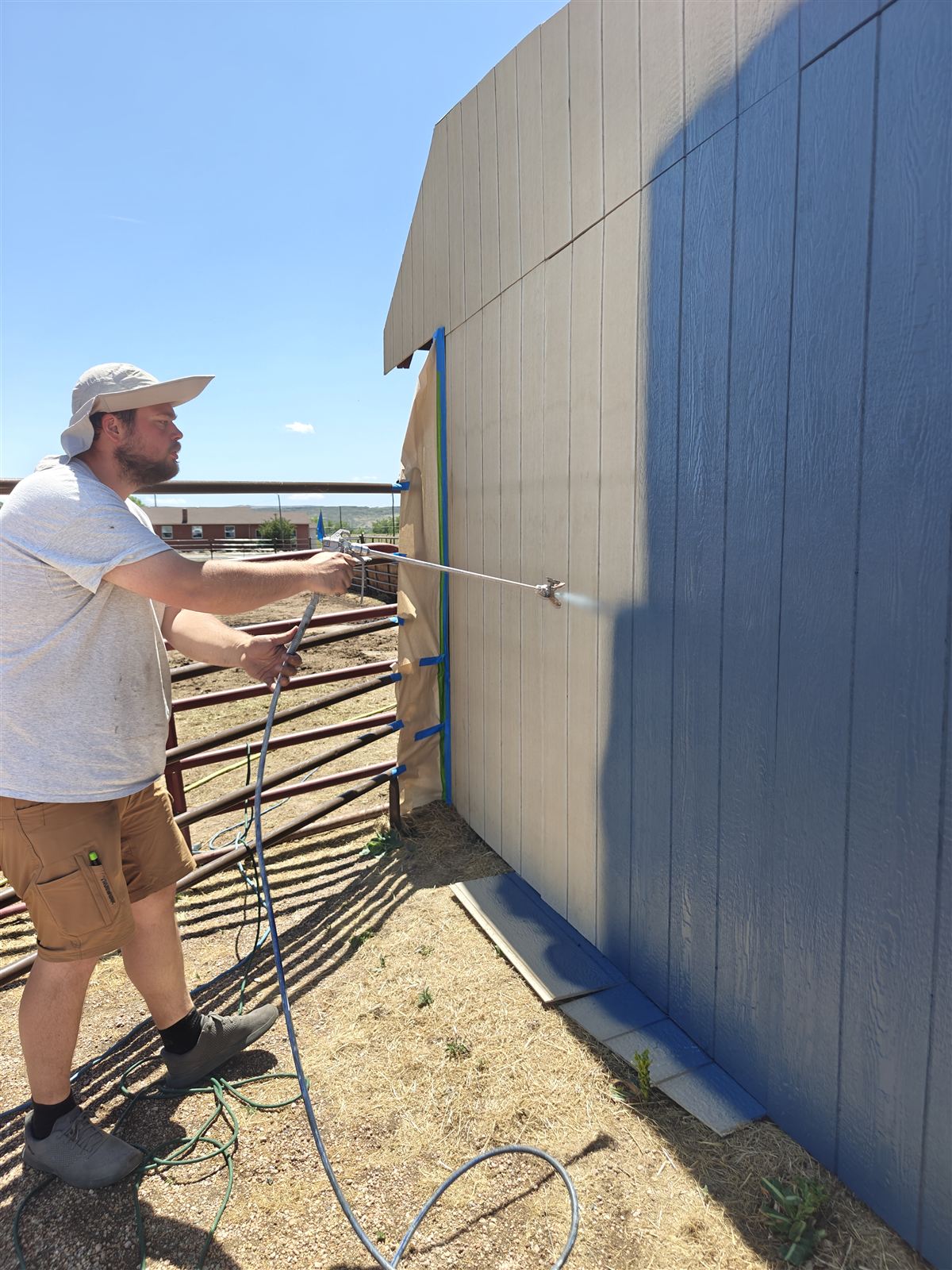 Painter spray-applying paint to house siding in Arvada, Colorado