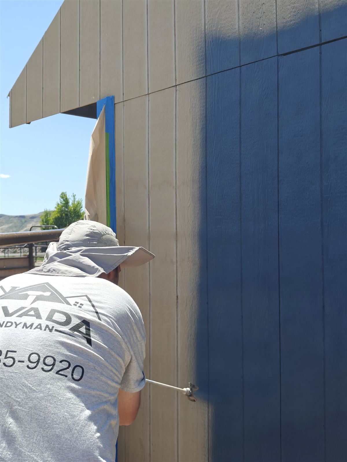 Painter in an Arvada Handyman shirt spray-applying the new siding color