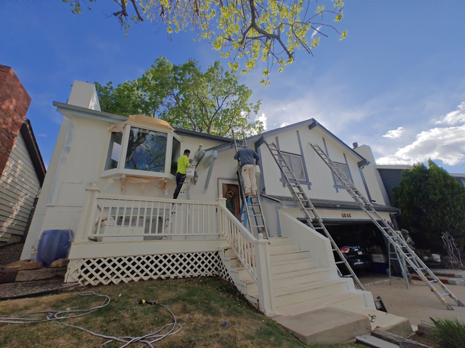 Two painters on ladders repainting the upper story and porch trim of a home exterior