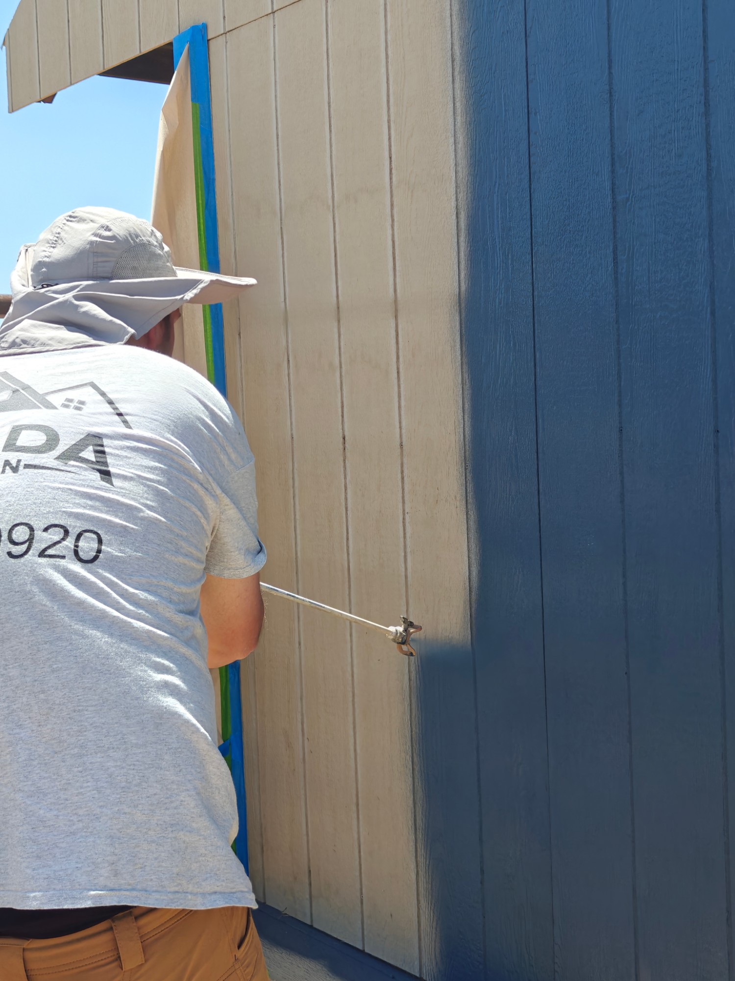 Painter airless-spraying blue paint onto new tan factory-primed LP SmartSide shed siding